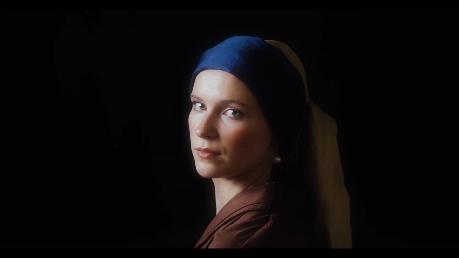 A man and a woman in a dim room, she wears a blue headscarf and a pearl earring (7/8)